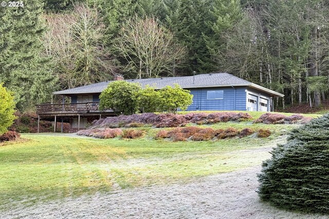 view of side of property featuring a chimney, a wooden deck, a garage, a view of trees, and a yard