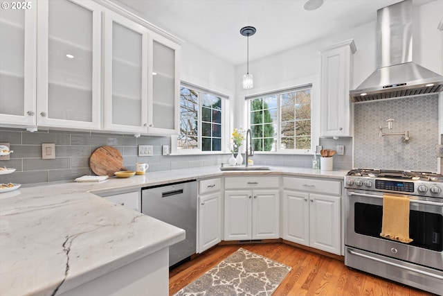 kitchen with wall chimney exhaust hood, sink, white cabinetry, hanging light fixtures, and appliances with stainless steel finishes