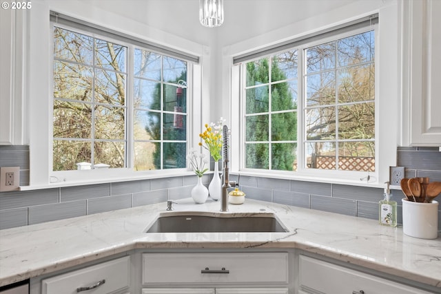 kitchen featuring tasteful backsplash, sink, white cabinets, and light stone counters