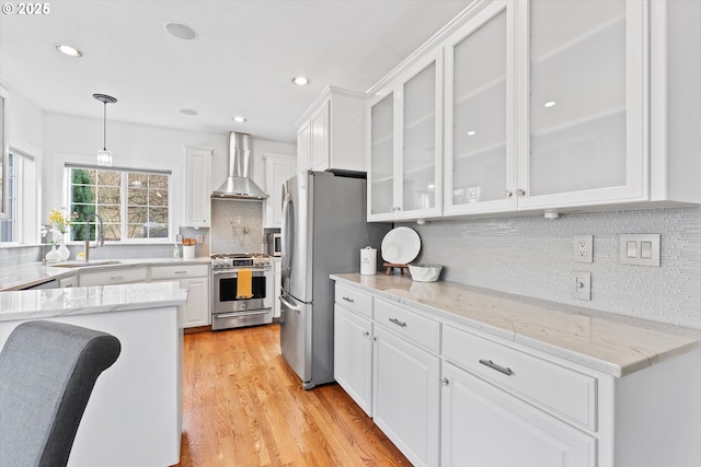 kitchen with hanging light fixtures, appliances with stainless steel finishes, white cabinets, and wall chimney exhaust hood