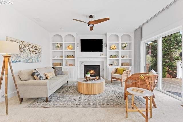 carpeted living room with ceiling fan, a fireplace, and built in features