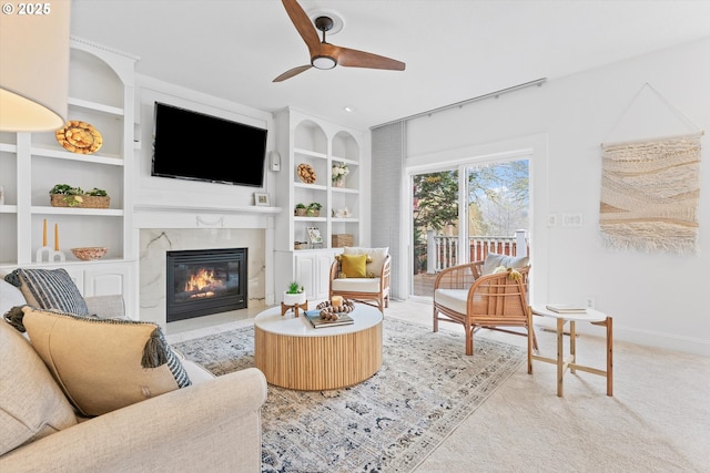 living room featuring a premium fireplace, carpet floors, built in features, and ceiling fan