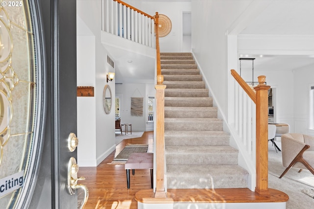 stairs with hardwood / wood-style flooring, a towering ceiling, and ornamental molding