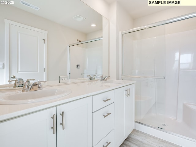 bathroom with a shower stall, double vanity, and wood finished floors