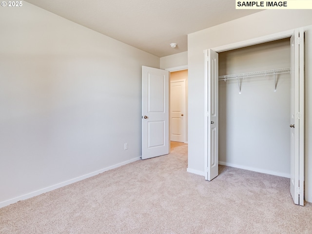 unfurnished bedroom with light carpet, baseboards, and a closet