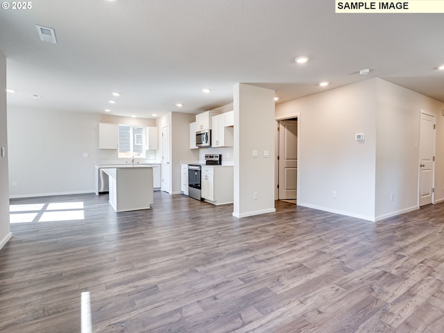 unfurnished living room featuring wood finished floors, baseboards, recessed lighting, and a sink