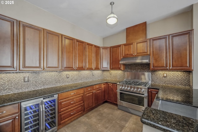 kitchen featuring stainless steel range, under cabinet range hood, wine cooler, dark stone countertops, and hanging light fixtures