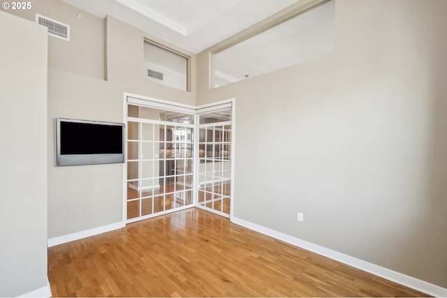 unfurnished room with wood finished floors, baseboards, and a high ceiling