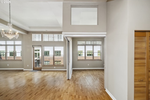 unfurnished living room featuring a chandelier, wood finished floors, baseboards, and a towering ceiling