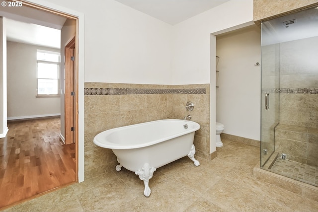 bathroom with a freestanding tub, a stall shower, toilet, tile walls, and a wainscoted wall