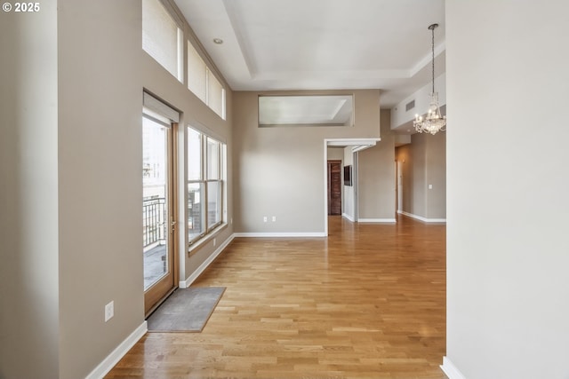 spare room with a chandelier, light wood-style floors, baseboards, and a raised ceiling