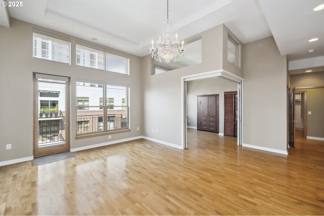spare room featuring a chandelier, light wood finished floors, baseboards, a towering ceiling, and recessed lighting