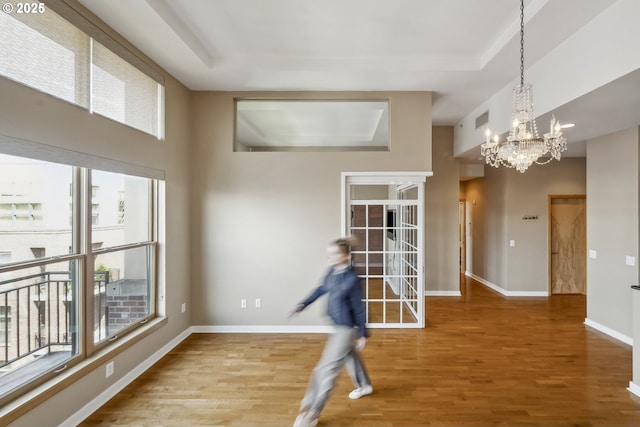 spare room with a chandelier, wood finished floors, baseboards, a tray ceiling, and a towering ceiling