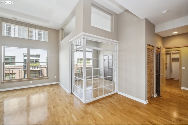 spare room with wood finished floors, baseboards, healthy amount of natural light, a high ceiling, and recessed lighting