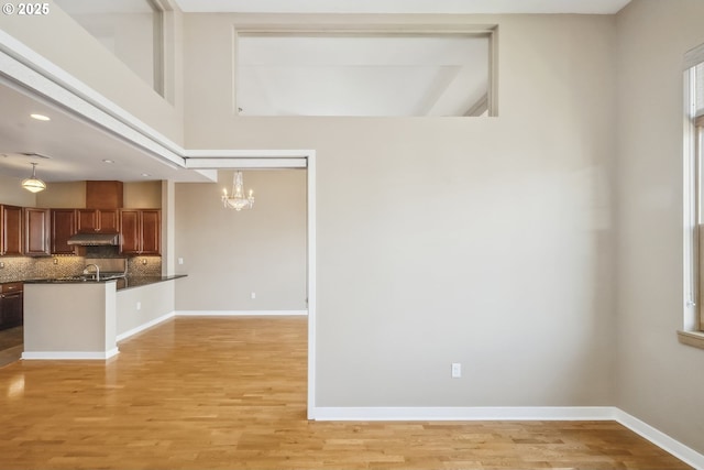 unfurnished living room with a chandelier, light wood-style flooring, and baseboards