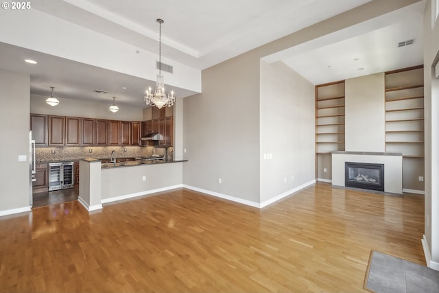 unfurnished living room featuring beverage cooler, a sink, light wood-type flooring, a chandelier, and baseboards