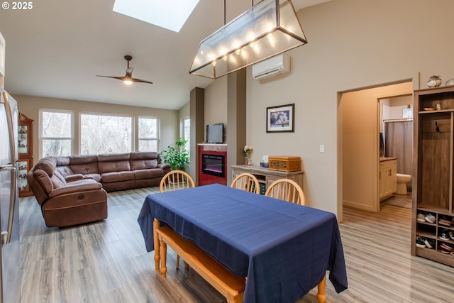 dining area featuring a glass covered fireplace, a wall unit AC, light wood-style floors, a skylight, and ceiling fan