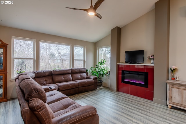 living room featuring light wood finished floors, a glass covered fireplace, a ceiling fan, and vaulted ceiling