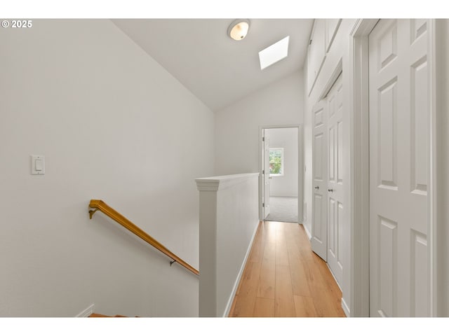 corridor featuring light wood-type flooring, baseboards, lofted ceiling, and an upstairs landing