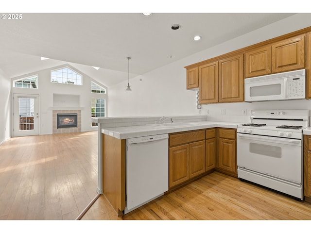 kitchen featuring vaulted ceiling, a sink, a peninsula, white appliances, and light wood-style flooring