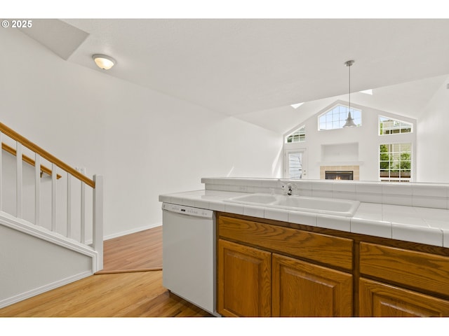 kitchen with brown cabinetry, dishwasher, a sink, light wood finished floors, and lofted ceiling with skylight