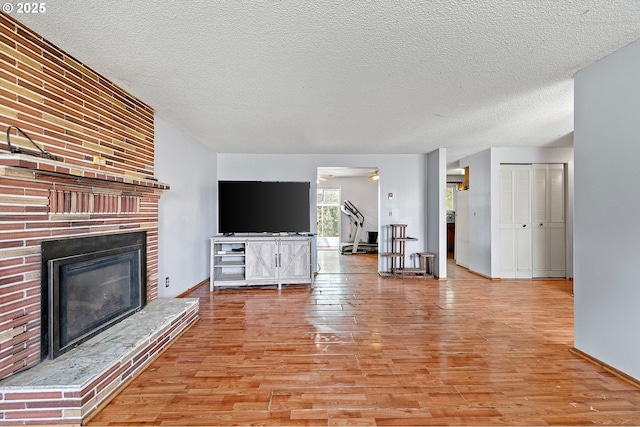 unfurnished living room with light wood-style floors, a textured ceiling, a fireplace, and baseboards
