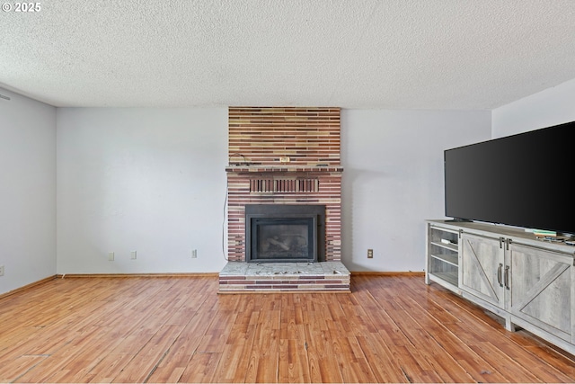unfurnished living room with a textured ceiling, wood finished floors, a fireplace, and baseboards