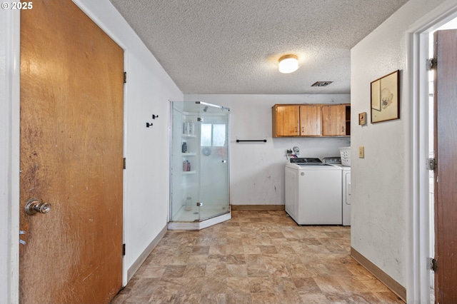 washroom featuring cabinet space, baseboards, washer and clothes dryer, a textured ceiling, and stone finish flooring