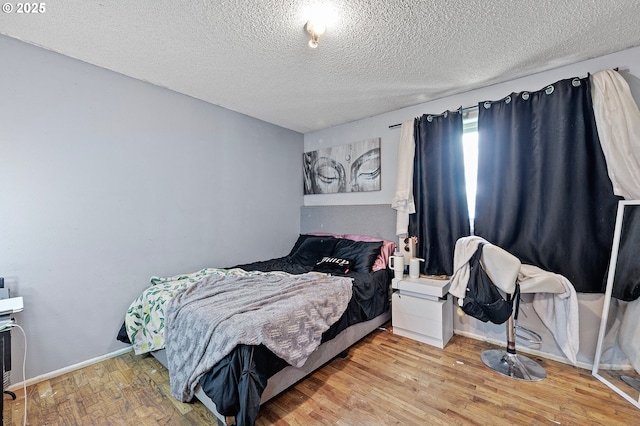 bedroom with a textured ceiling, wood finished floors, and baseboards