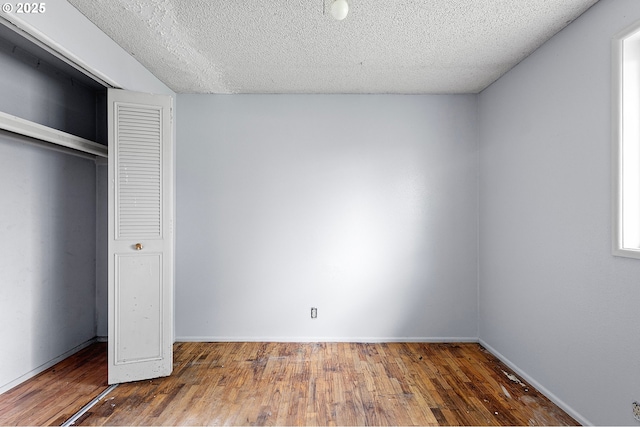 unfurnished bedroom featuring wood finished floors, a textured ceiling, a closet, and baseboards