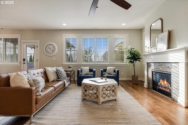 living room featuring a textured ceiling, ceiling fan, wood-type flooring, and a fireplace