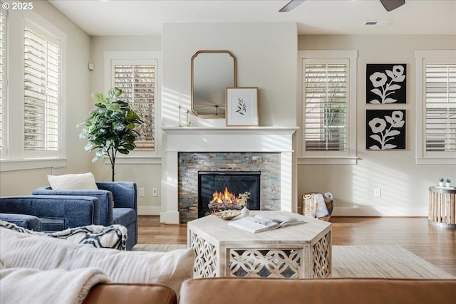 living room with a stone fireplace, a wealth of natural light, and light wood-type flooring