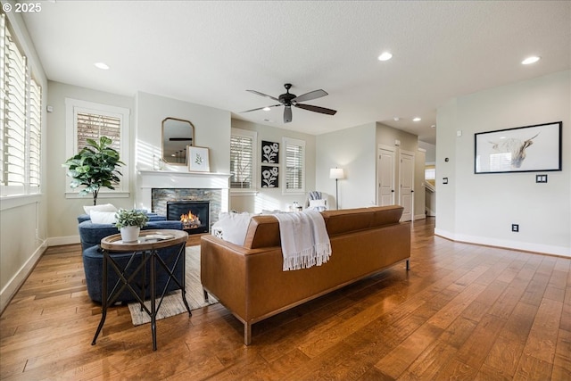 living room featuring hardwood / wood-style flooring, ceiling fan, a stone fireplace, and a textured ceiling