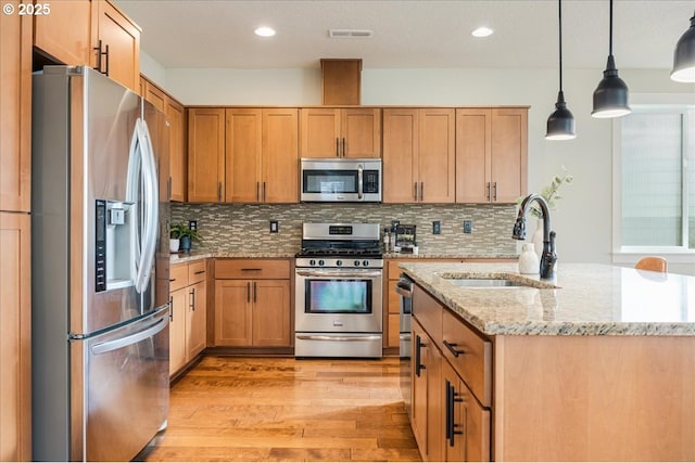 kitchen with decorative backsplash, appliances with stainless steel finishes, light stone countertops, sink, and pendant lighting