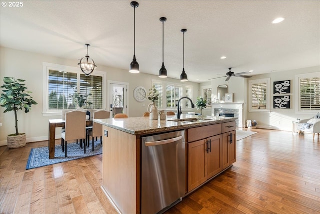 kitchen with light stone countertops, dishwasher, sink, a fireplace, and a center island with sink