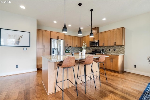 kitchen featuring light hardwood / wood-style floors, a center island with sink, pendant lighting, and appliances with stainless steel finishes