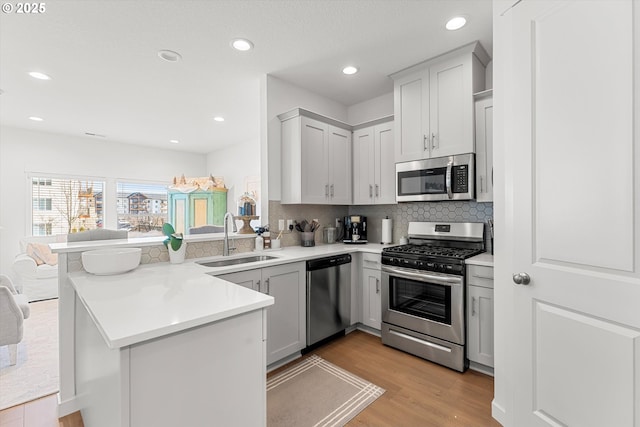 kitchen with a sink, light wood-style floors, appliances with stainless steel finishes, a peninsula, and decorative backsplash