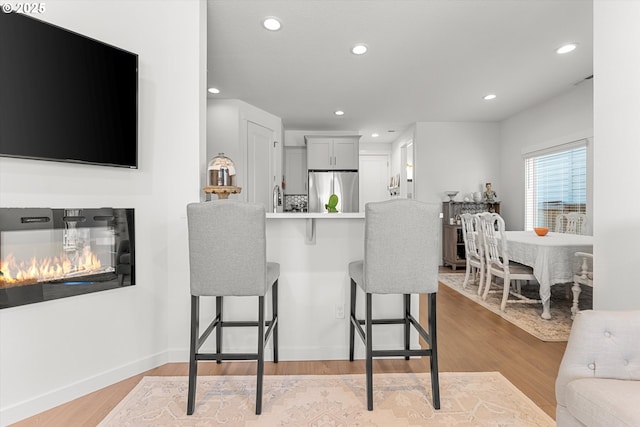 kitchen with recessed lighting, a kitchen breakfast bar, stainless steel fridge, and light wood-style floors