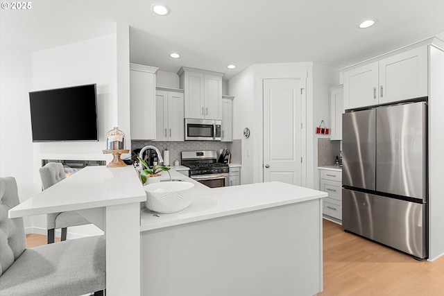 kitchen with light wood finished floors, light countertops, decorative backsplash, a peninsula, and stainless steel appliances