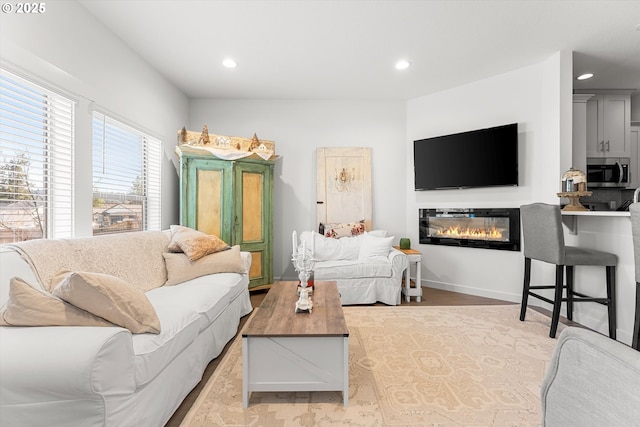 living room with a glass covered fireplace, wood finished floors, recessed lighting, and baseboards