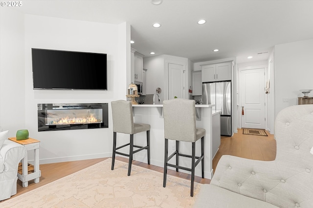 kitchen with light wood-type flooring, gray cabinets, light countertops, a kitchen bar, and stainless steel fridge