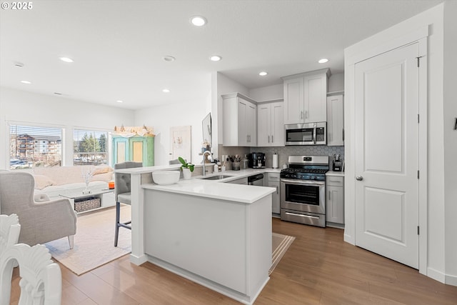 kitchen with wood finished floors, a peninsula, a sink, light countertops, and appliances with stainless steel finishes