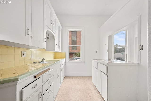 kitchen featuring sink, white cabinetry, light tile patterned flooring, decorative backsplash, and tile countertops