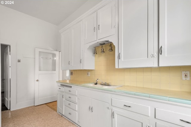 kitchen featuring white cabinetry, tile countertops, sink, and decorative backsplash