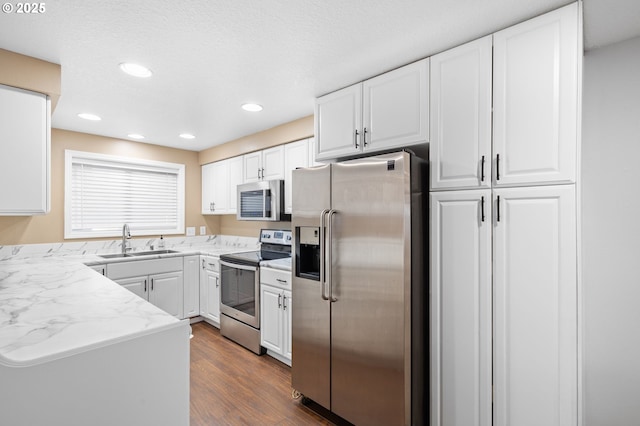 kitchen with sink, appliances with stainless steel finishes, dark hardwood / wood-style floors, light stone counters, and white cabinets