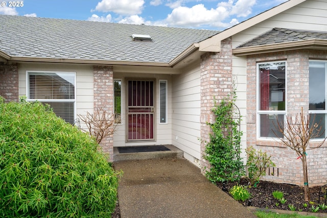 view of exterior entry featuring crawl space, roof with shingles, and brick siding