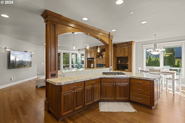 kitchen featuring kitchen peninsula, stainless steel gas cooktop, hardwood / wood-style flooring, a chandelier, and hanging light fixtures