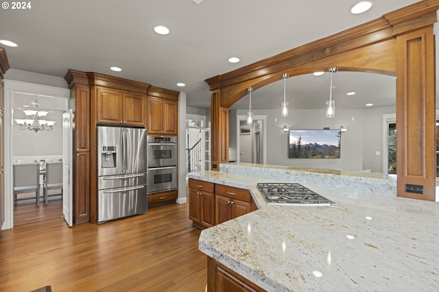 kitchen with pendant lighting, an inviting chandelier, appliances with stainless steel finishes, light stone counters, and wood-type flooring