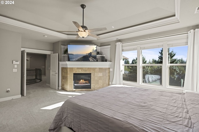 carpeted bedroom featuring a tray ceiling, ceiling fan, and a tiled fireplace