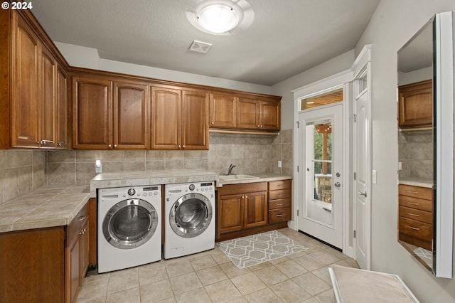 laundry room with cabinets, a textured ceiling, sink, washer and dryer, and light tile patterned floors